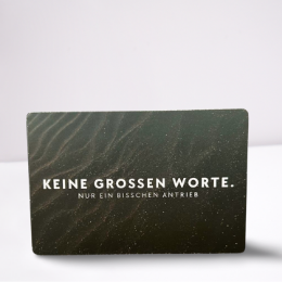 Schwarze Geschenkverpackung mit dem weißen Schriftzug "Keine großen Worte. Nur ein bisschen Antrieb"
